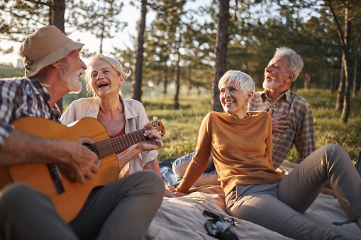 Happy mature couples enjoying in guitar music during picnic in nature.