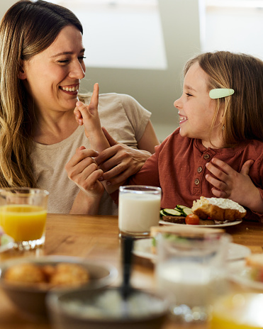 Happy mother communicating with her small girl during breakfast in dining room.