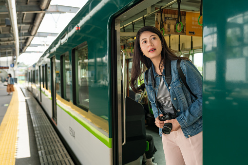 curious asian Chinese girl passenger leaning out from car and looking into distance while waiting for the green train to depart at platform of uji station in Kyoto japan