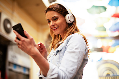 Beautiful blonde woman with headphones. Young smiling woman listening the music outside