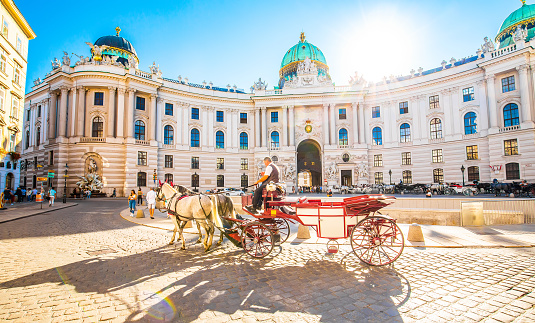 Vienna, Austria - 19 June, 2022: Scenic travel photo of Hofburg Palace and horse carriage on sunny Wien street