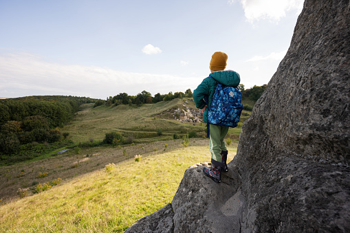 Boy with backpack climbing big stone in hill. Pidkamin, Ukraine.