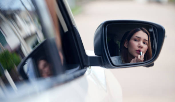 istock Young woman applying lipstick looking at reflection in car mirror. 1438075692