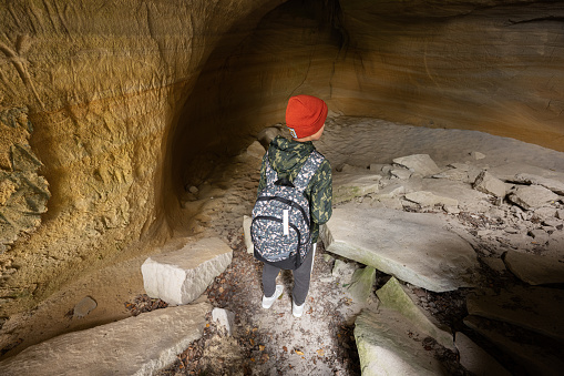 Boy wear backpack explore limestone stone cave at mountain in Pidkamin, Ukraine.