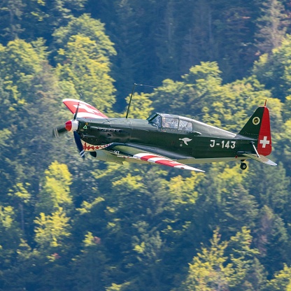 Gruyere, Switzerland – September 04, 2022: A view of Morane-Saulnier M.S.406 fighter aircraft flying over the trees in Aerodrome Epagny