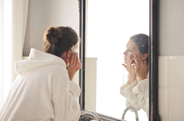 istock Young female looking in the mirror and touching her face skin 1438079165