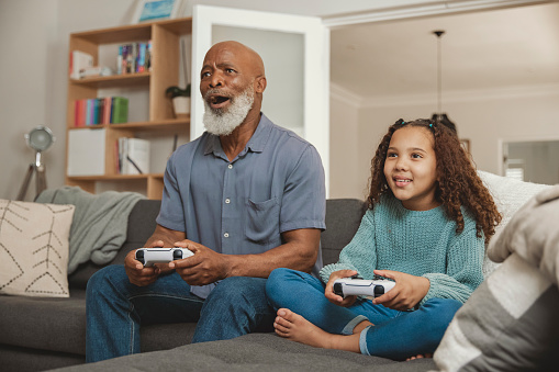 Senior man playing video games with his granddaughter while bonding on the sofa at home