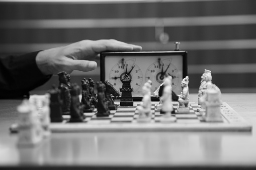 A grayscale closeup shot of a hand setting off the timer near a chessboard