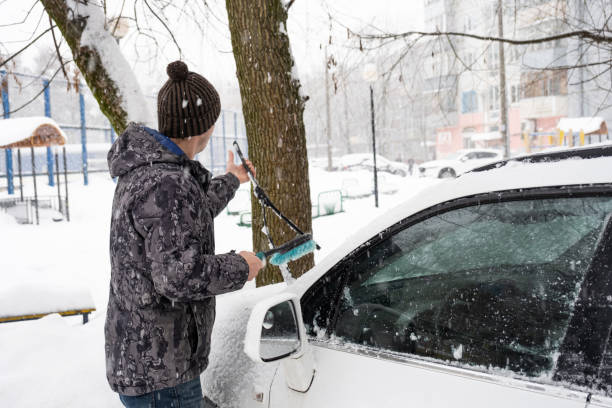 un uomo spazzola la neve da un'auto dopo una nevicata. sicurezza stradale, condizioni meteorologiche difficili in inverno - snow car window ice scraper foto e immagini stock
