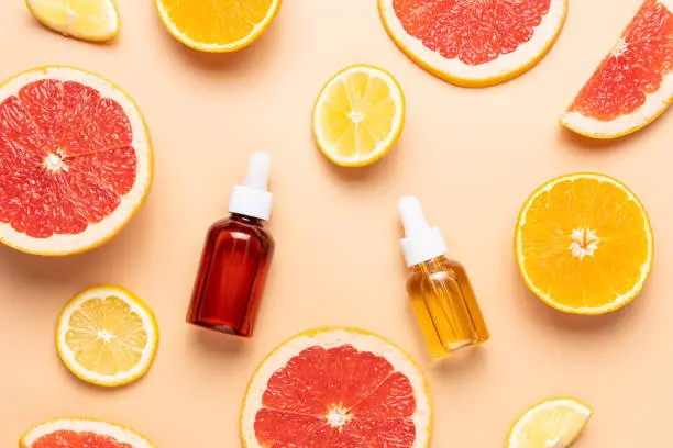 Slice of grapefruit, orange, lemon and set of cosmetic bottles on beige background, top view
