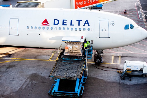 Amsterdam, Netherlands – May 14, 2020: A closeup of people loading cargo into the Delta airplane at Schiphol Amsterdam Airport