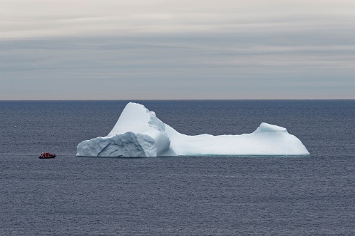 A small tour boat next to a large iceberg, Newfoundland and Labrador, Canada.