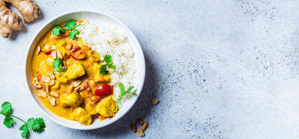 Thai chicken and peanut curry with rice in a white bowl, gray background, top view, copy space. stock photo