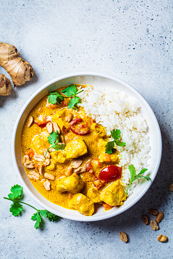 Thai chicken and peanut curry with rice in a white bowl, gray background, top view. Asian cuisine concept.