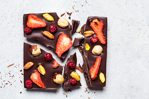 Vegan homemade dark chocolate with berries and nuts on white paper, top view.