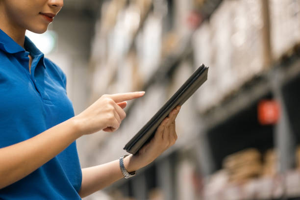 istock Young female worker in blue uniform checklist manage parcel box product in warehouse. Asian woman employee holding tablet working at store industry. Logistic import export concept. 1438089485