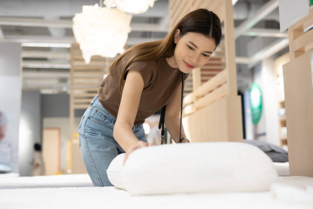 young beautiful woman choosing pillow at retail furniture store. housewife pick up the pillow and softness test buying for family. female checking quality shopping at mattress store hall. - furniture store furniture retail textile imagens e fotografias de stock