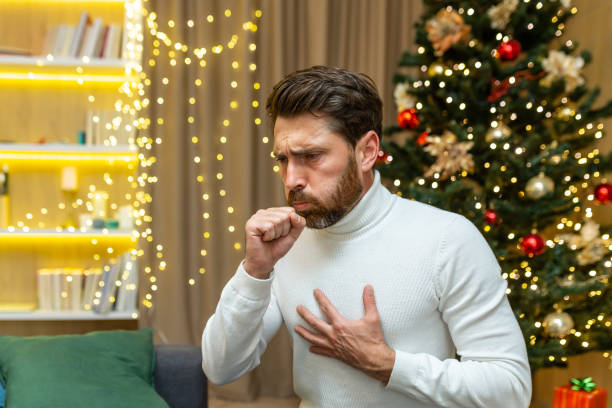 man coughs on christmas at home sitting alone on sofa sick on new year holidays in living room man coughs on christmas at home sitting alone on sofa sick on new year holidays in living room. painfully stock pictures, royalty-free photos & images
