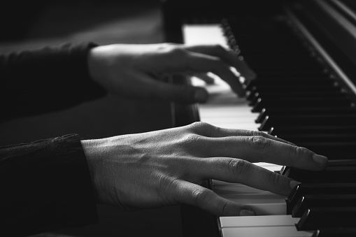 Two hands on a piano keyboard, black and white photo