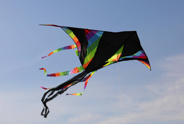 black kite with multicolored rainbow stripes flies high in the blue sky tied to a string