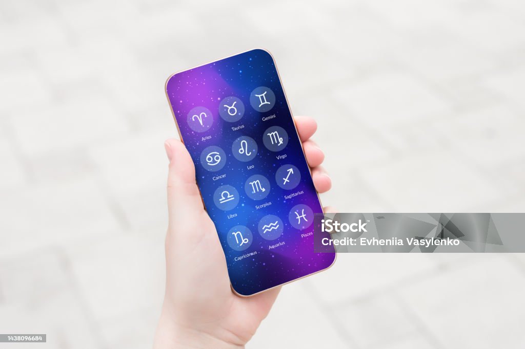 female hand shows a mobile phone with an astrological application with zodiac signs female hand shows a mobile phone with an astrological application with zodiac signs. forecast for zodiac signs for the day Adult Stock Photo