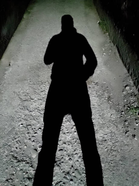 istock Man casting a shadow against a lamp post in a dark alley at night. India. 1438097834