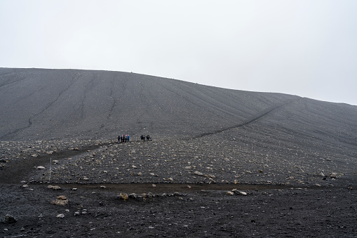 Small group of tourists hiking up the huge Hverfjall volcanic crater on cloudy day.  Hverfjall, is one of the best preserved circular volcanic craters in the world and it is possible to walk around and inside it.