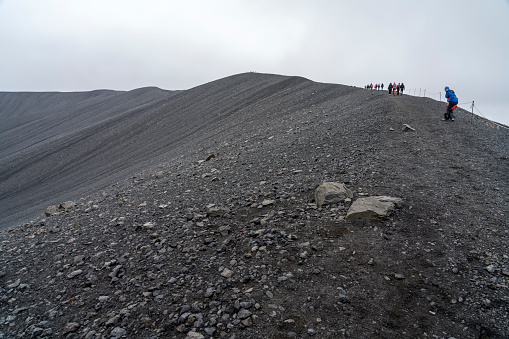Small group of tourists hiking the edge of huge Hverfjall volcanic crater on cloudy day.  Hverfjall, is one of the best preserved circular volcanic craters in the world and it is possible to walk around and inside it.