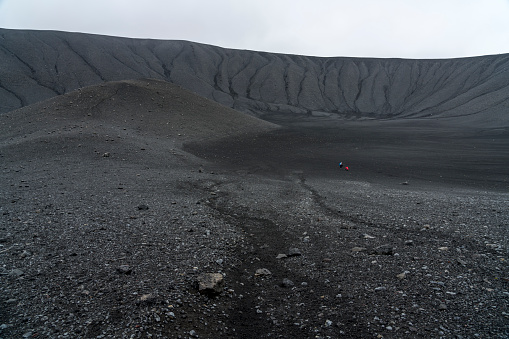 Two women down at the bottom of the Hverfjall volcanic crater on cloudy day.  Hverfjall, is one of the best preserved circular volcanic craters in the world and it is possible to walk around and inside it.