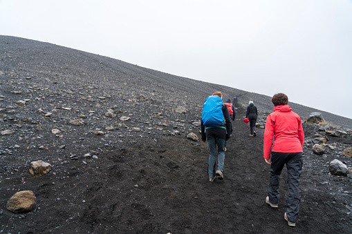 Small group of tourists hiking the path up the huge Hverfjall volcanic crater on cloudy day.  Hverfjall, is one of the best preserved circular volcanic craters in the world and it is possible to walk around and inside it.