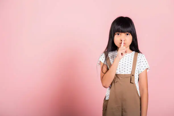 Child secret. Asian kid 10 years old holding finger on lips symbol of hush gesture of asking quiet at studio shot isolated on pink background, Happy children girl show shh with finger at mouth gossip