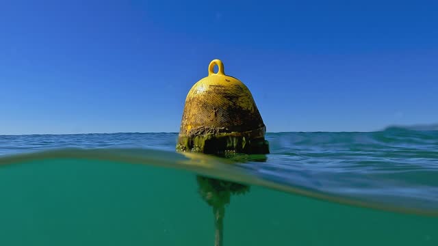 Half underwater tilt up view from seafloor to surface of yellow floating mooring buoy on seawater. Slow motion