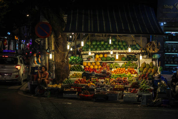 um vendedor ambulante em uma barraca de frutas colorida iluminada por lâmpadas - vietnam asia hanoi street - fotografias e filmes do acervo