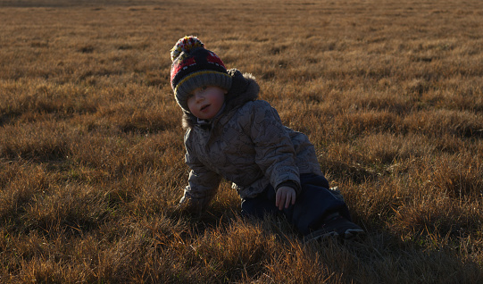 Little boy lies on his side on the brown autumn grass and looks at the camera