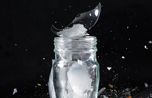 A closeup shot of small glass jar with broken pieces on dark background