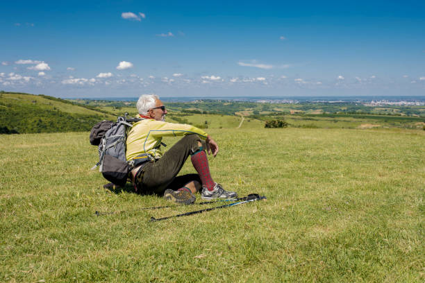 A handsome old man sitting on a meadow and looking relaxing after a hike