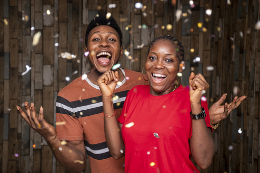 Two happy African people celebrating with confetti in front of a wooden wall