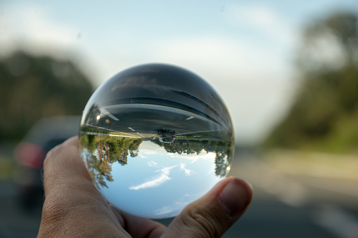 A closeup shot of a person holding a crystal ball with the reflection of trees, road, and the sky