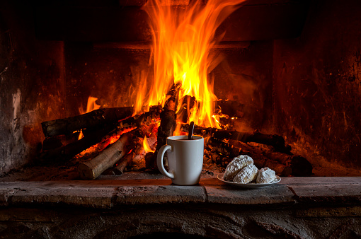 New Year and Christmas composition. National, Christmas greek cookies kourabies and a cup of coffee close-up against the background of a burning fireplace