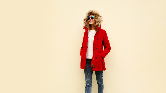 Stylish smiling young woman wearing red coat jacket with fur hood walking looking away on background, blank copy space for advertising text