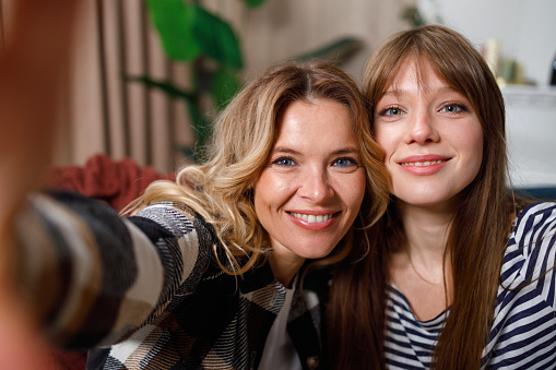 Portrait of cute mother and adult daughter who taking selfie at home