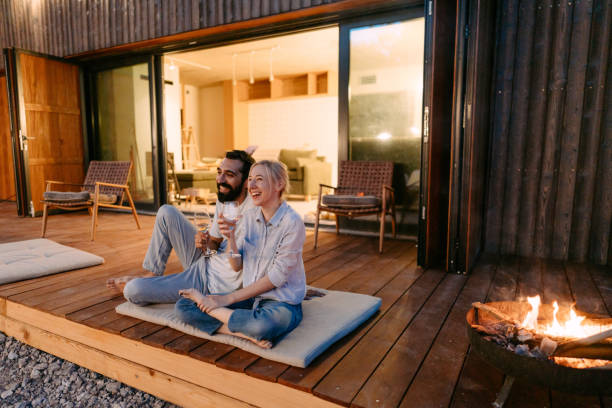 Young couple drinking wine by the fire pit Photo of a young couple drinking wine by the fire pit in front of the cabin house airbnb stock pictures, royalty-free photos & images