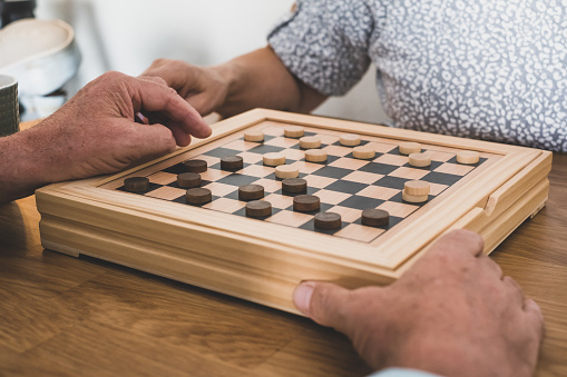 Two senior people at home while playing a game of checkers on wooden table.
