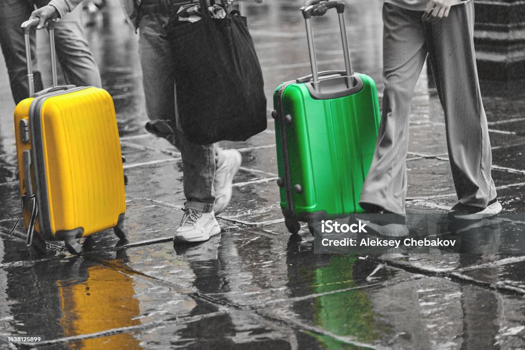 Tourists travel around the city with a green and yellow suitcase in the rain Tourists travel around the city with a green and yellow suitcase in the rain. Arrival Stock Photo