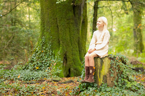 Ten year old blonde wearing a skirt suit and boots in the woods.