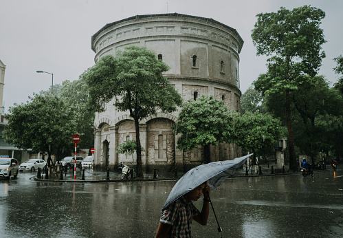 A cityscape or city view in the modern city of Hanoi Vietnam, where people holding umbrella are walking in front of the ancient architecture or historical building \