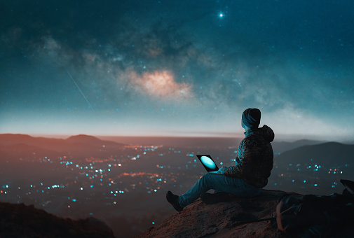 mature latin man sitting on top of a hill above a city with laptop looking at the milky way, valle del elqui