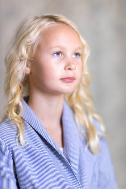 Close up of a young blonde preteen girl with neutral expression on a white studio background