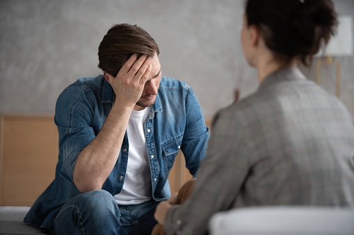 Psychologist talking with patient on therapy session. Depressed man speaking to a therapist while she is taking notes