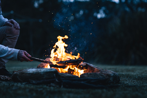 A man putting a log in a bonfire in the evening